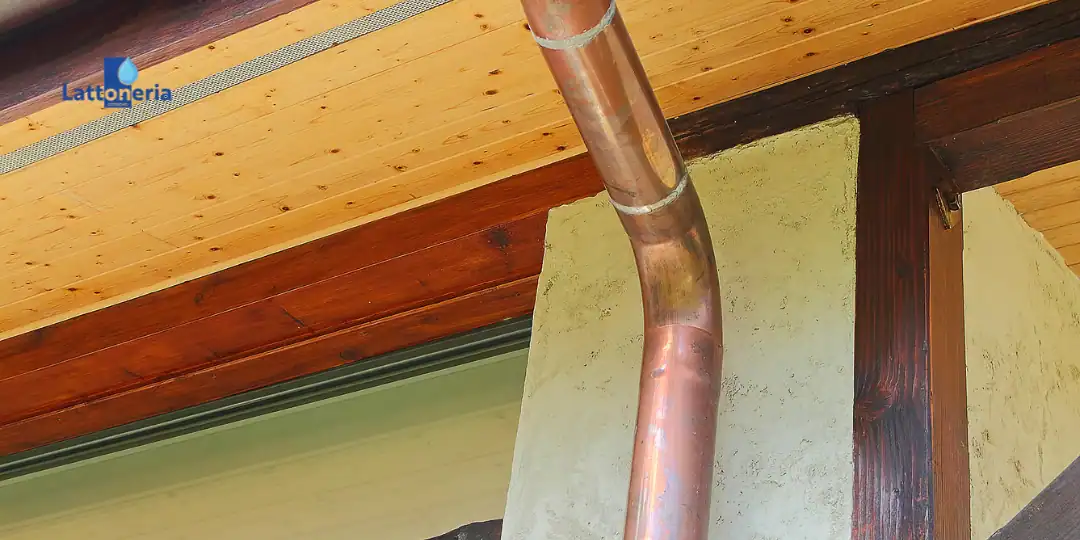 Tubo pluviale in rame da 100 mm installato sotto tetto in legno, dettaglio di curva e fissaggi.