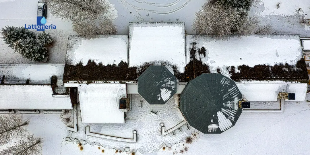 Vista dall’alto di edificio con coperture innevate e zone di scioglimento, utile per controllare accumuli di neve e deflusso (logo Lattoneria).